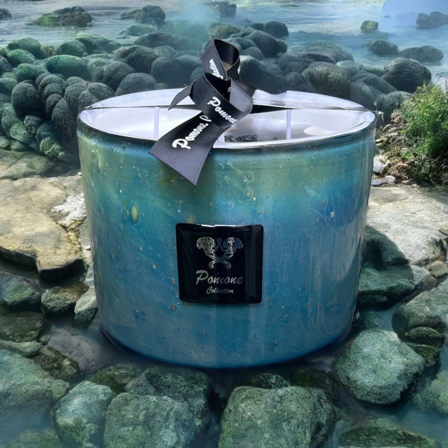Bougie bleu claire, turquoise et bleu foncée, posée sur des pierres dans un fond d'eau, vue de face