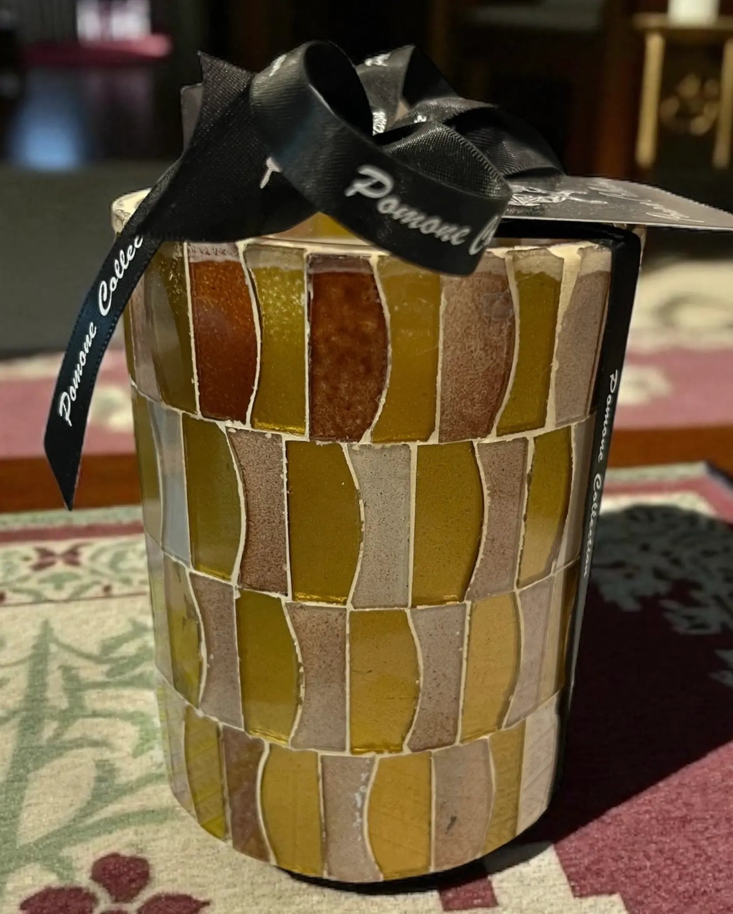 Bougie dorée, nude et bordeaux clair, posée sur un tapis, vue de face 