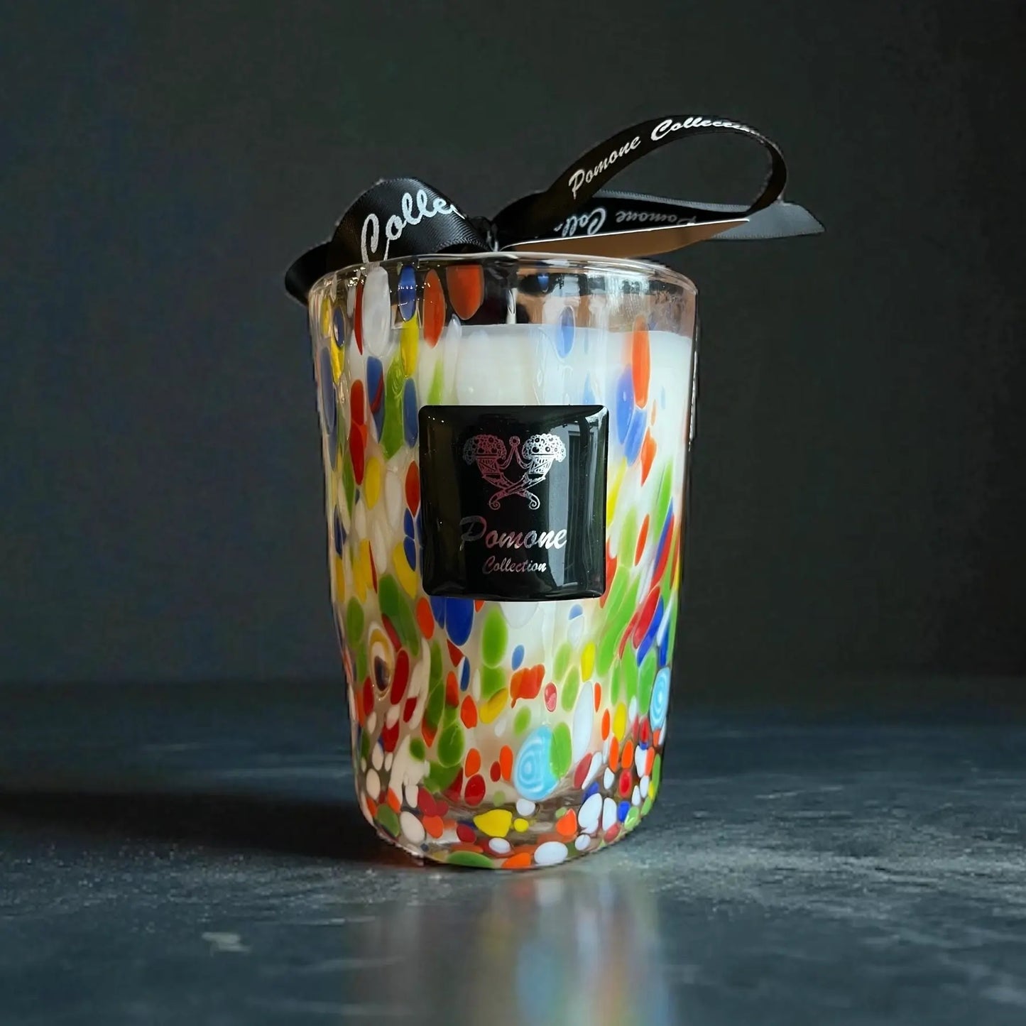 Bougie blanche et multicolore, vue de face avec ruban et étiquette sur fond noir