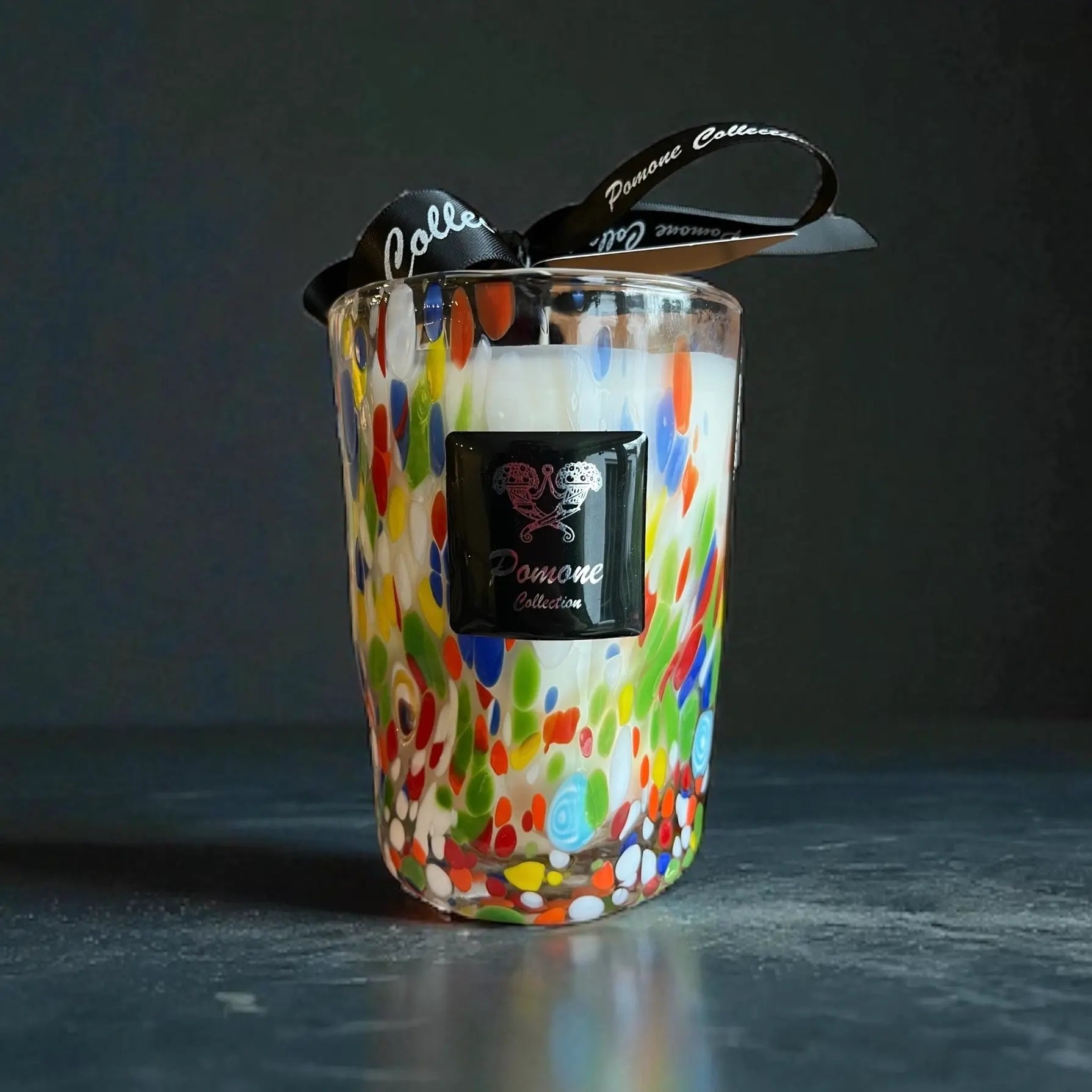 Bougie blanche et multicolore, vue de face avec ruban et étiquette sur fond noir