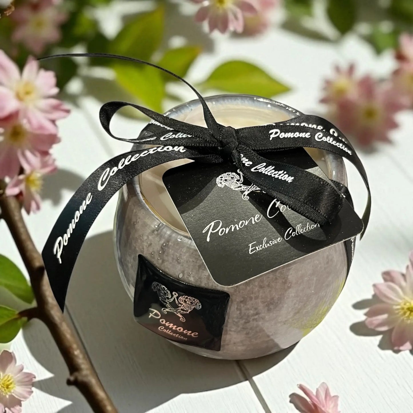 Bougie arrondie couleur parme gris, vue de haut avec ruban et étiquette sur fond blanc avec des fleurs