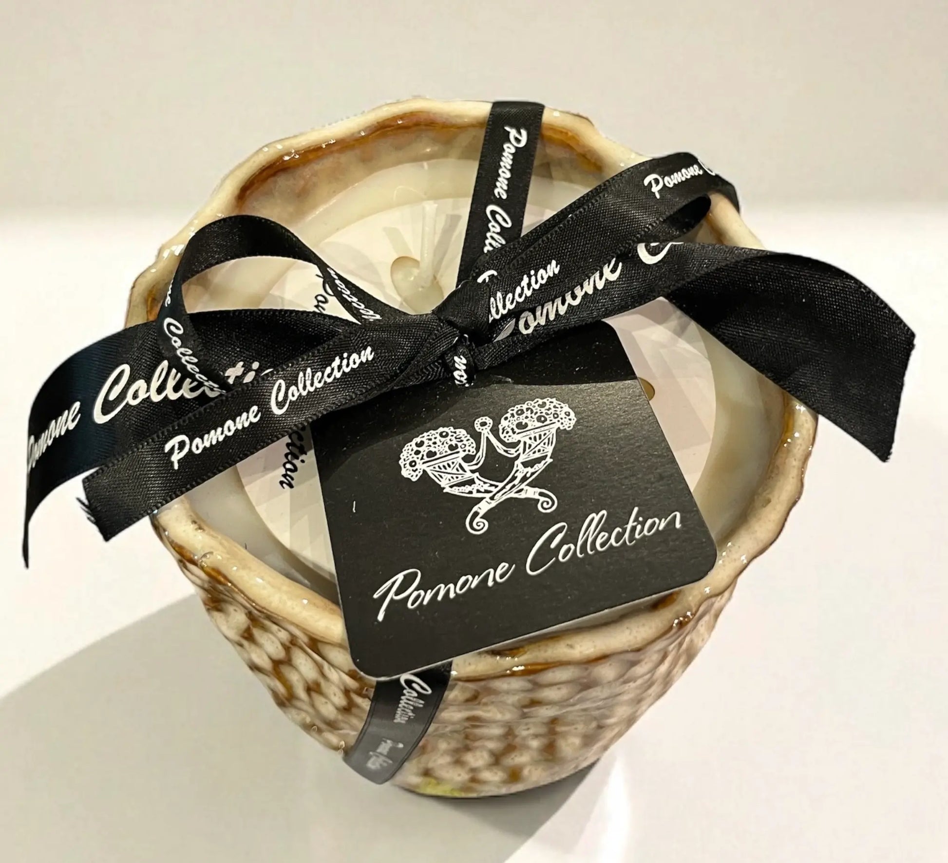 Bougie en céramique beige et blanc cassé, vue de haut avec ruban et étiquette