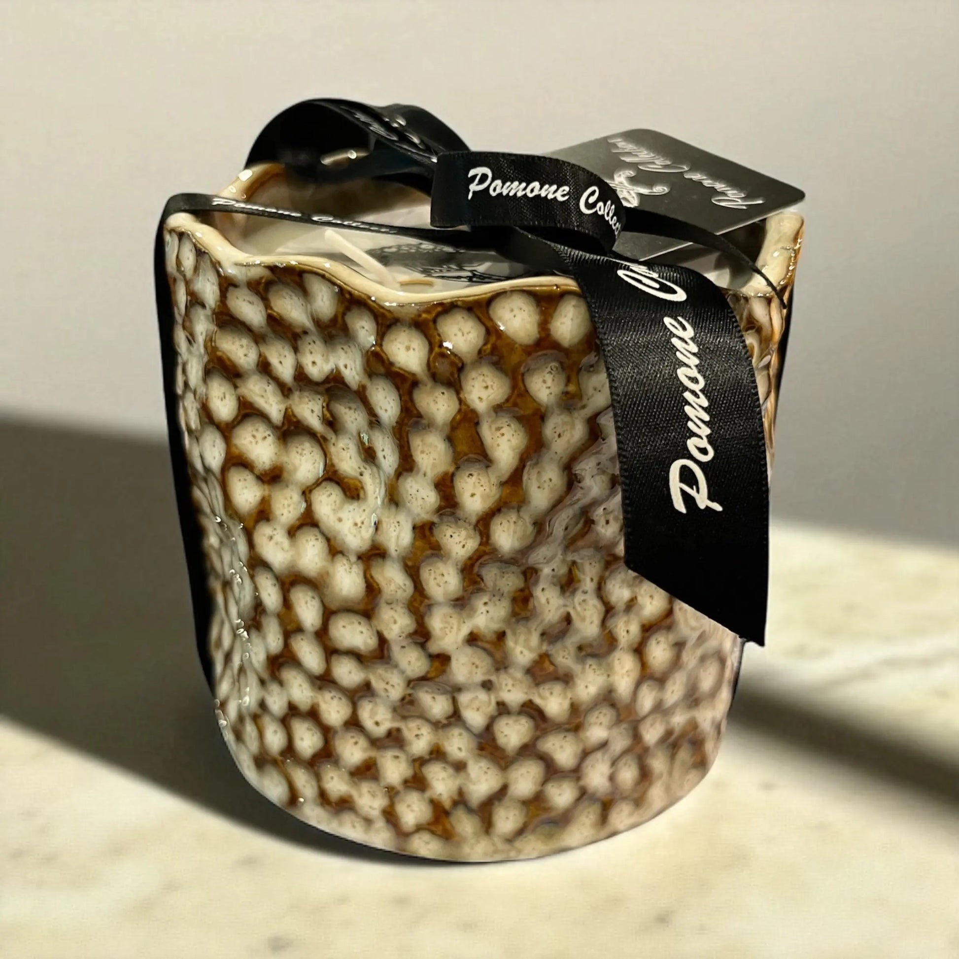 Bougie en céramique beige et blanc cassé, vue de face sur marbre beige