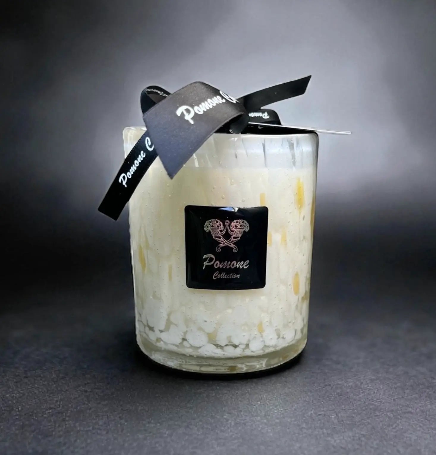 Bougie blanc cassé et jaune avec ruban et étiquette, vue de face sur fond noir