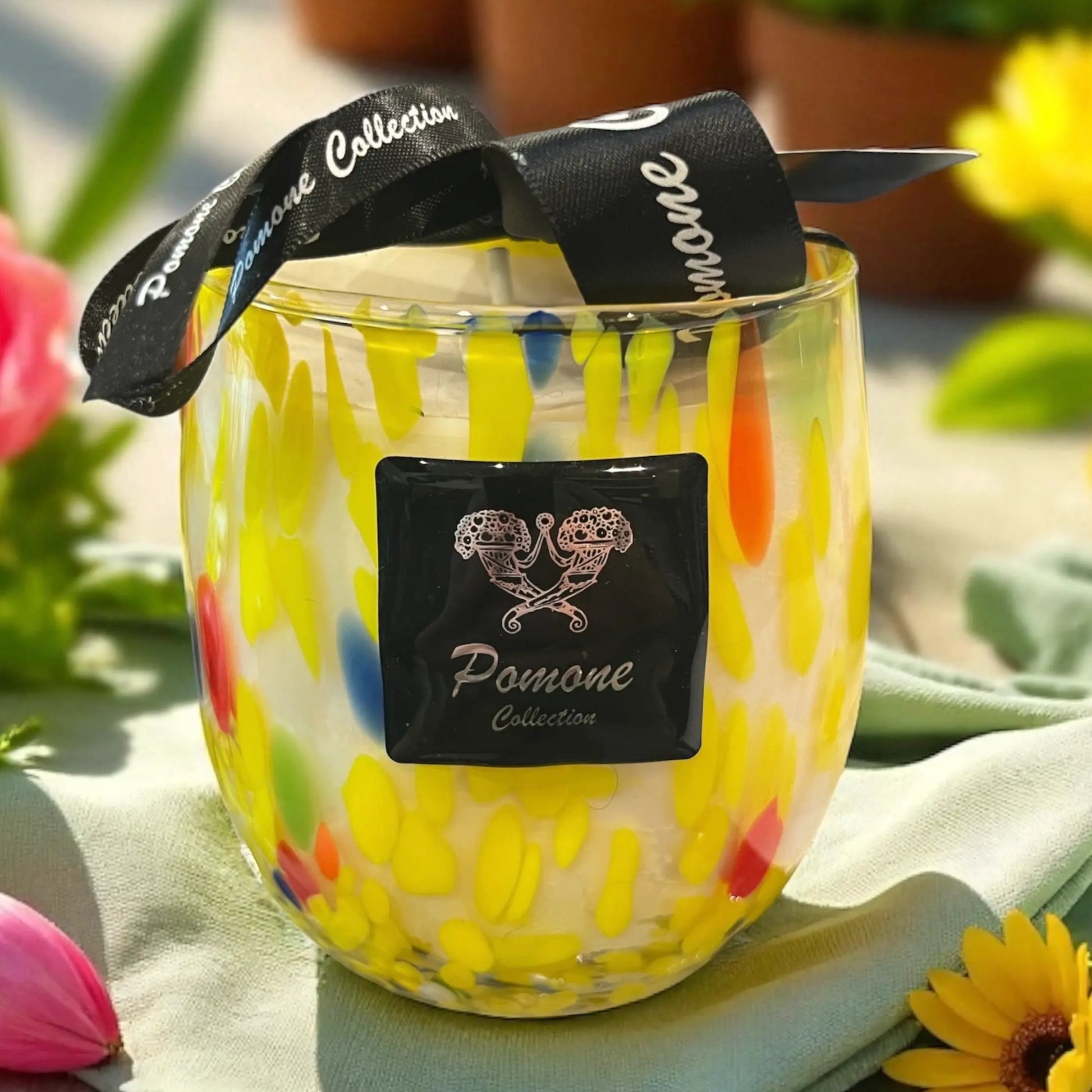 Bougie jaune avec une touche de rouge bleu et vert, aux côtés de fleurs, vue de face