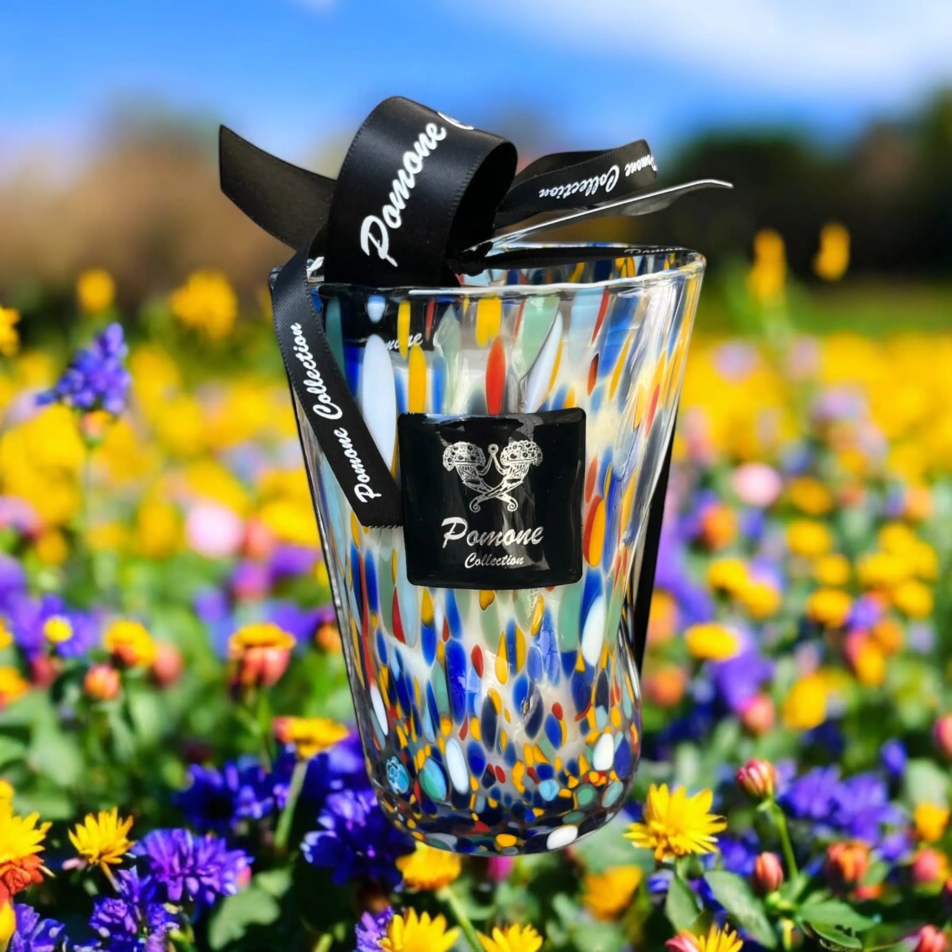 Bougie bleue tacheté orange, rouge et vert, vue de face avec un arrière plan de fleurs