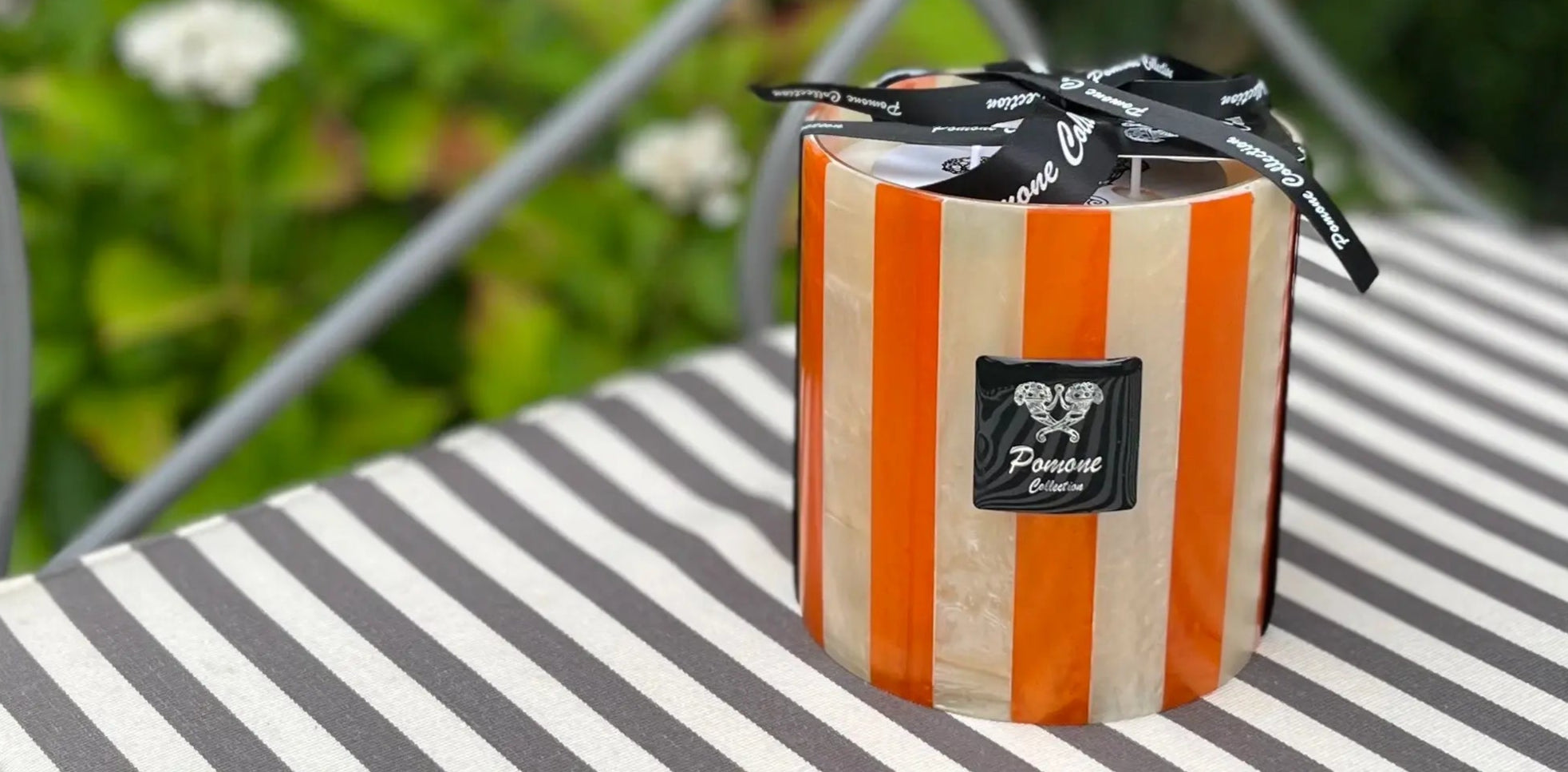 Bougie lignée orange et blanc crème sur coussin rayé dans un jardin