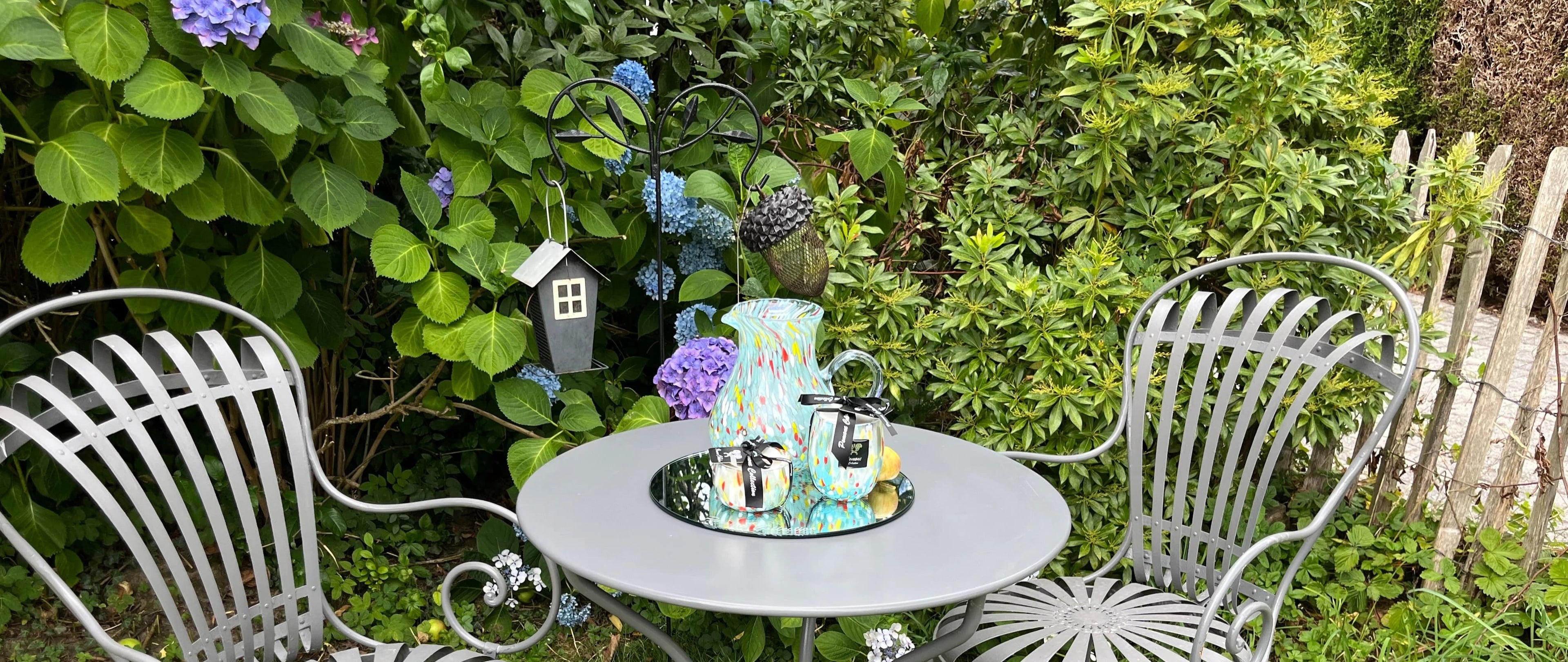 Deux bougies et une carafe multicolores sur table grise dans un jardin