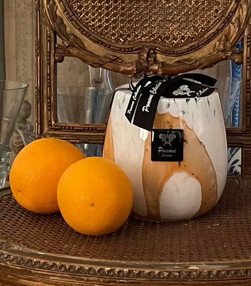 Bougie blanche et et brune claire, posée sur une chaise brune avec deux oranges