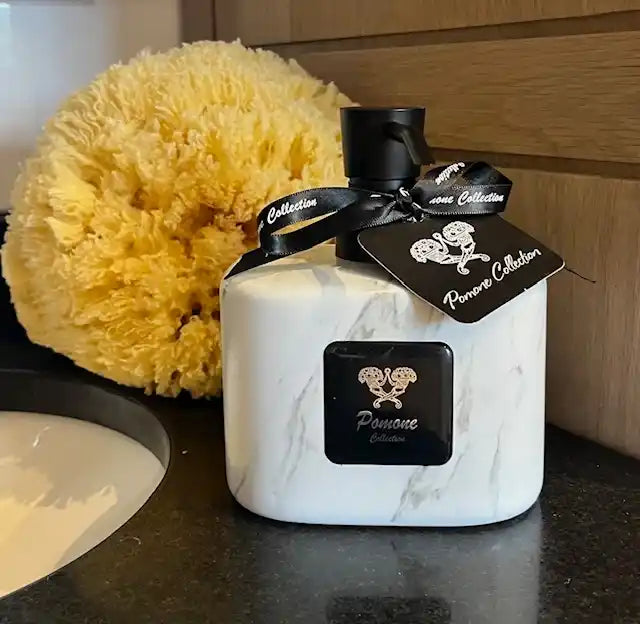 Bouteille de savon liquide couleur marbré blanc, vue de face sur marbre noir avec une éponge